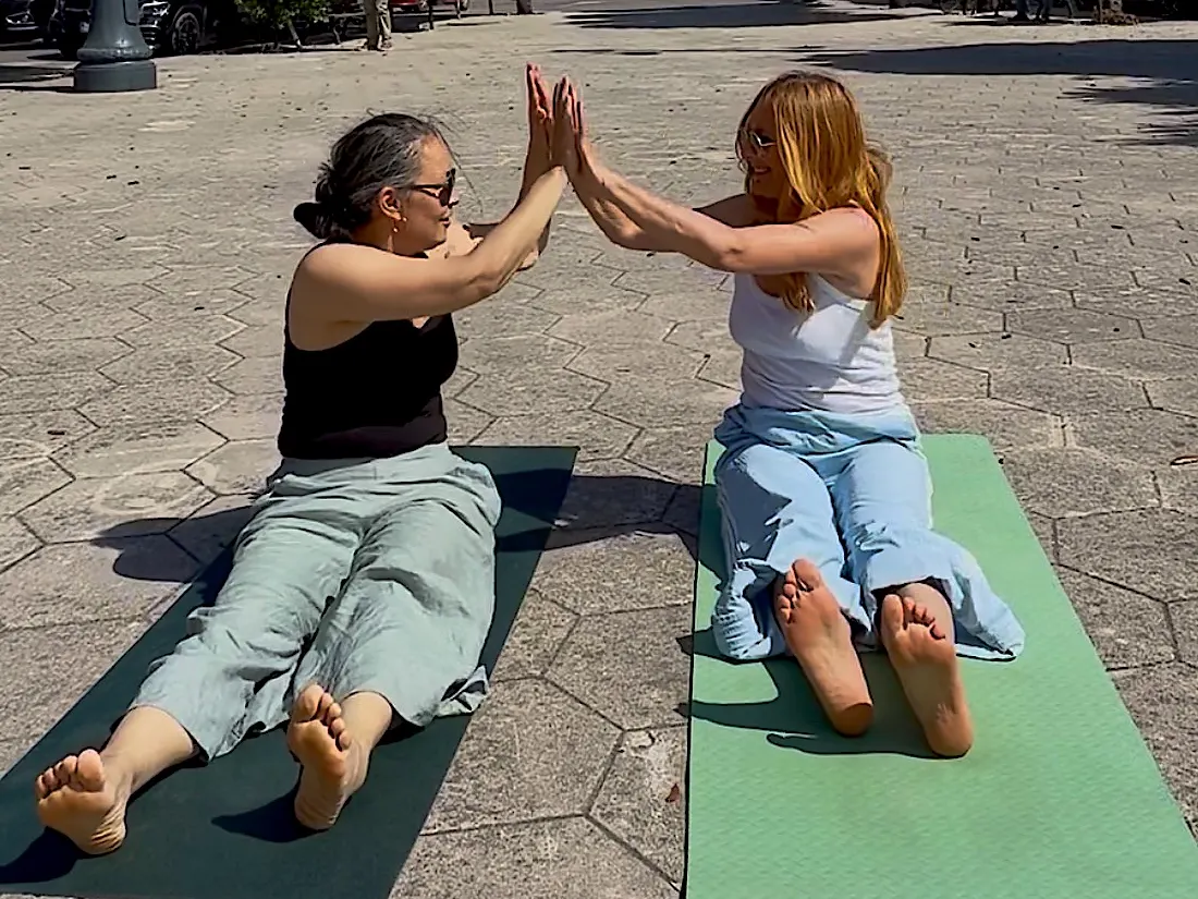 Sonia und Jeanna sitzen auf ihren Matten und berühren sich mit den Händen